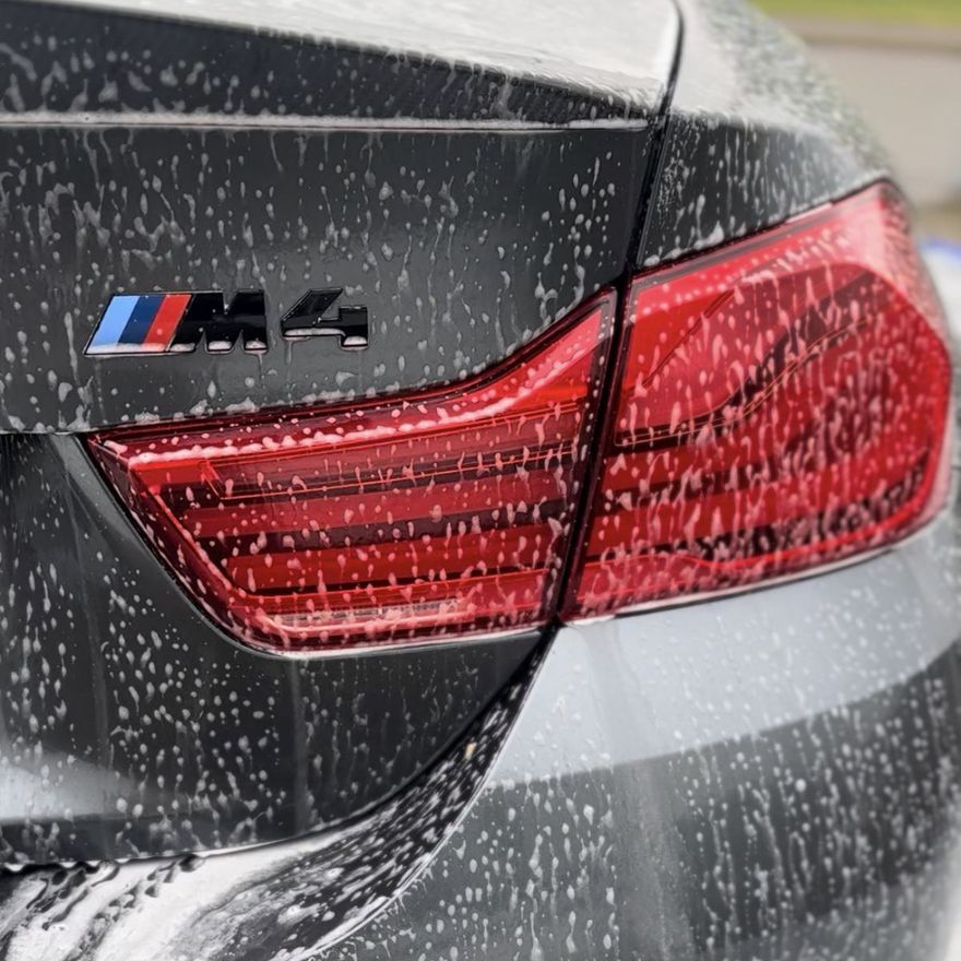 Bakparti med M4-emblem på en grå BMW täckt av tvättskum under utvändig rekond